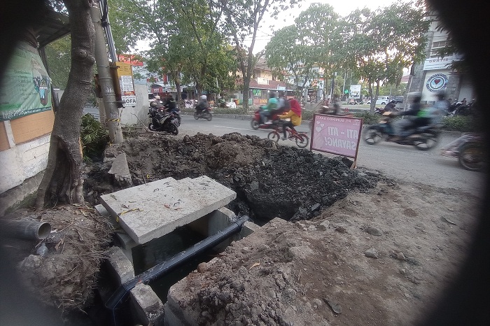 ATASI GENANGAN: Pengendara kendaraan bermotor melintas tak jauh dari proyek saluran di Jalan Mulyosari, Surabaya, Senin (29/7). (SURYANTO/RADAR SURABAYA)