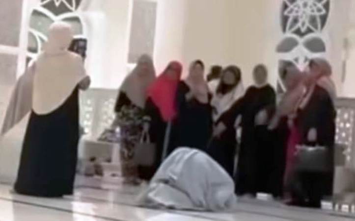 Rombongan emak emak yang asyik berfoto di dalam masjid di depan orang salat.