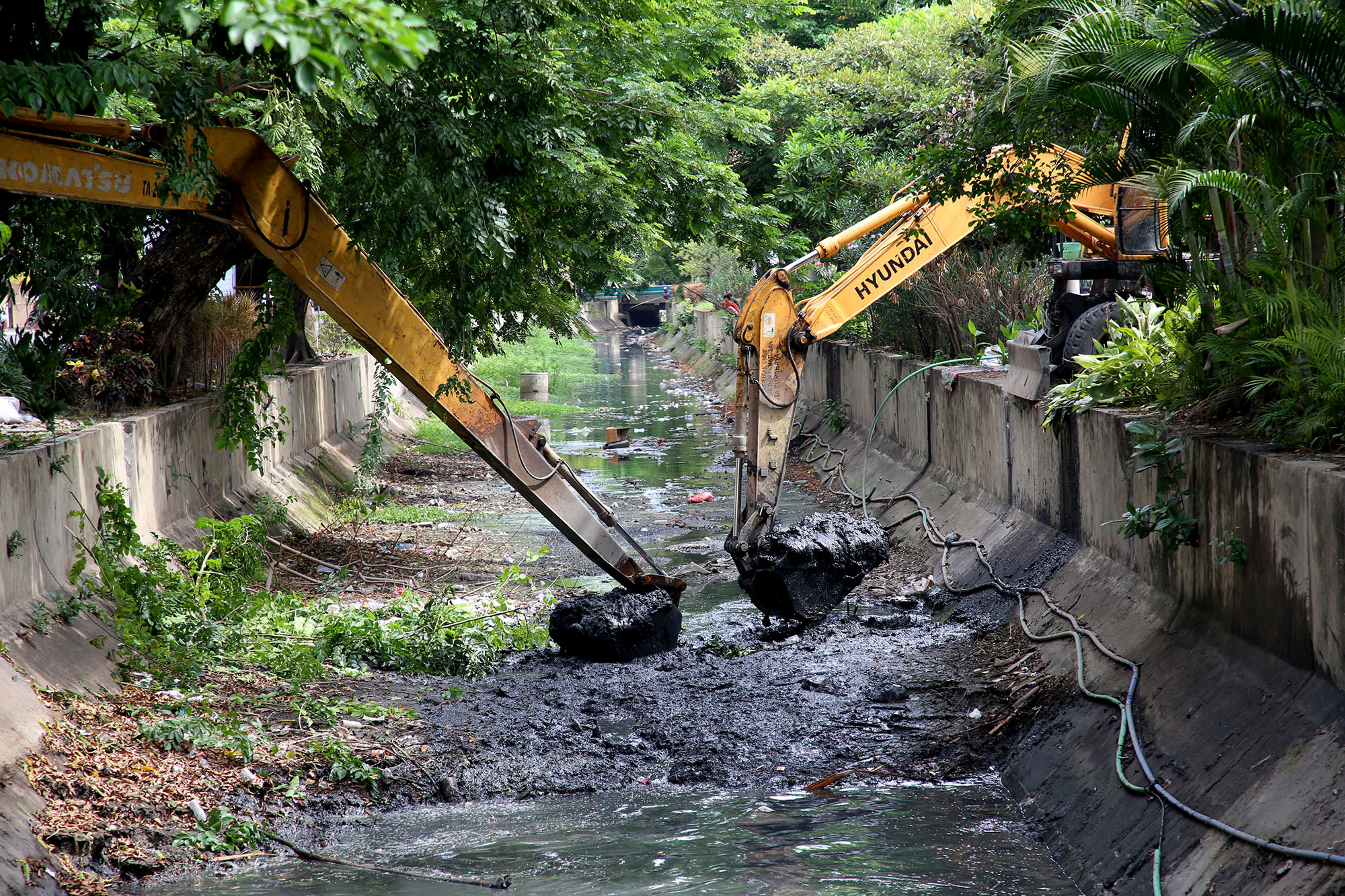 Ekskavator melakukan normalisasi saluran dengan pengerukan sedimen di saluran kawasan pusat kota Surabaya.