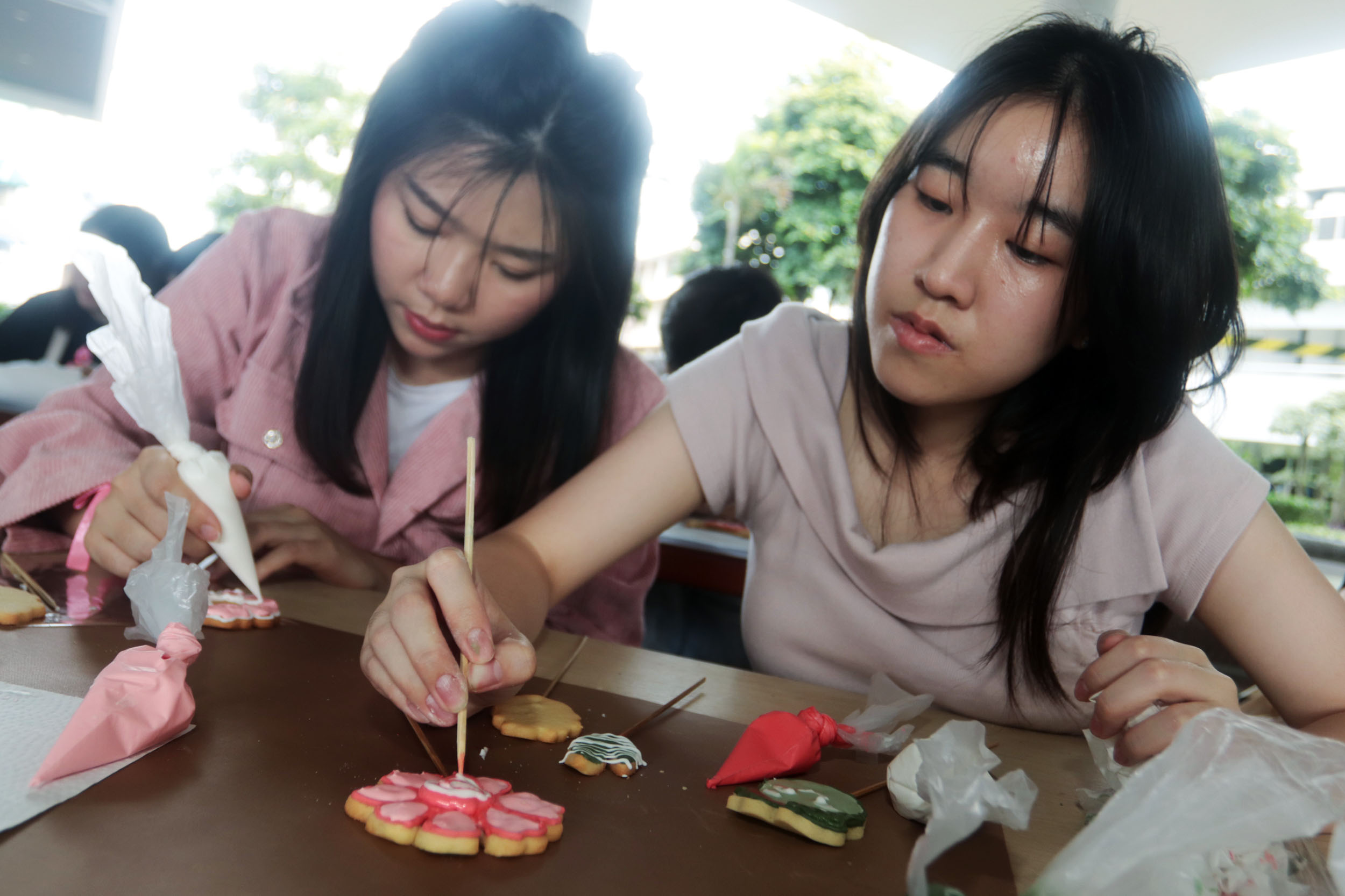 DEKORASI KUE: Evelyn Aurellia (kiri) dan Sherleen Felicia mahasiswa PCU Surabaya, melakukan dekorasi kue dengan berbagai warna untuk menyambut perayaan Hari Valentine.