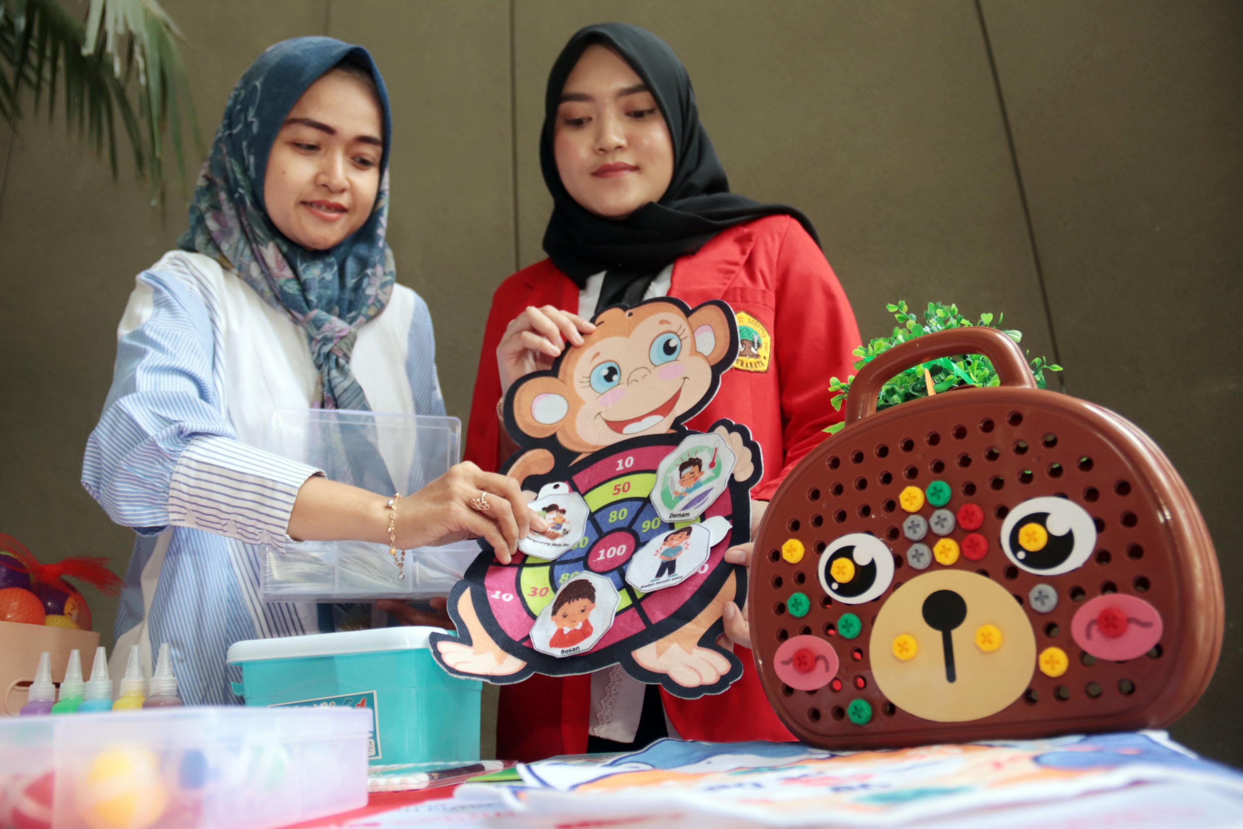 Assakinah Siscahyaningsih (kiri) disamping dosen pembimbingnya, menunjukkan cara bermain alat permainan sebagai terapi anak penderita kanker.
