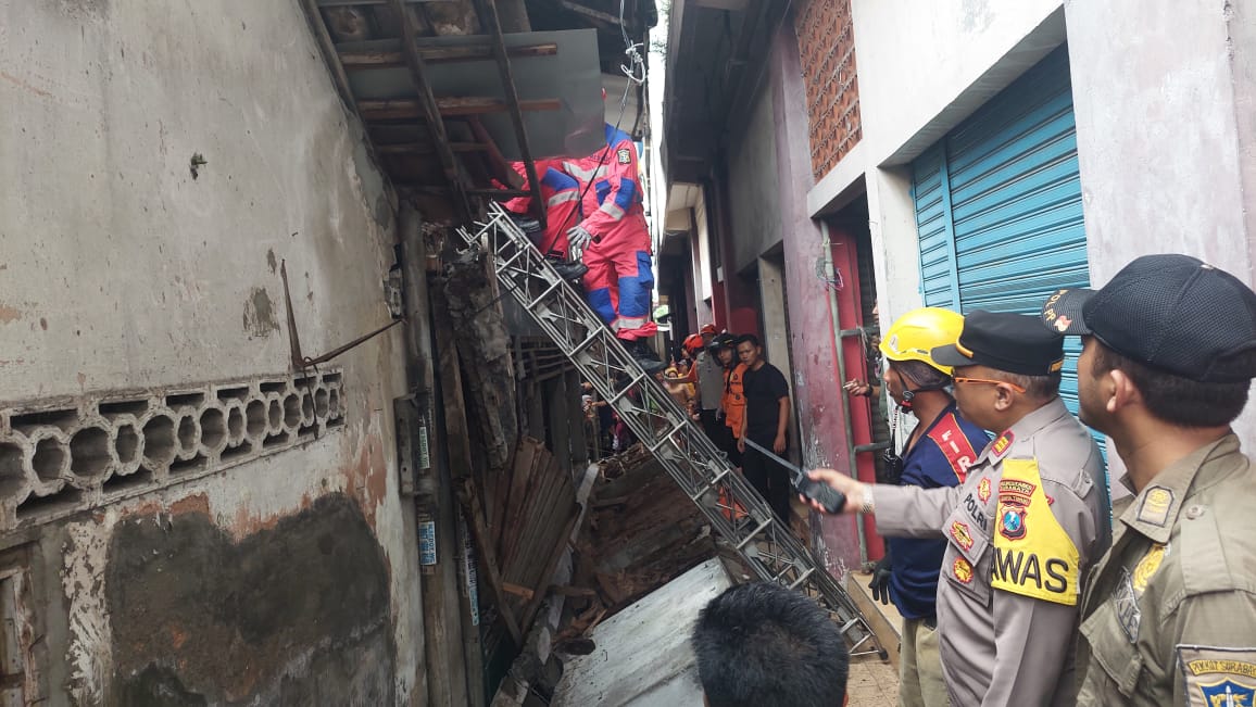 Petugas gabungan saat melakukan evakuasi mayat korban yang tertimpa tembok rumah di Putat Jaya, Surabaya.