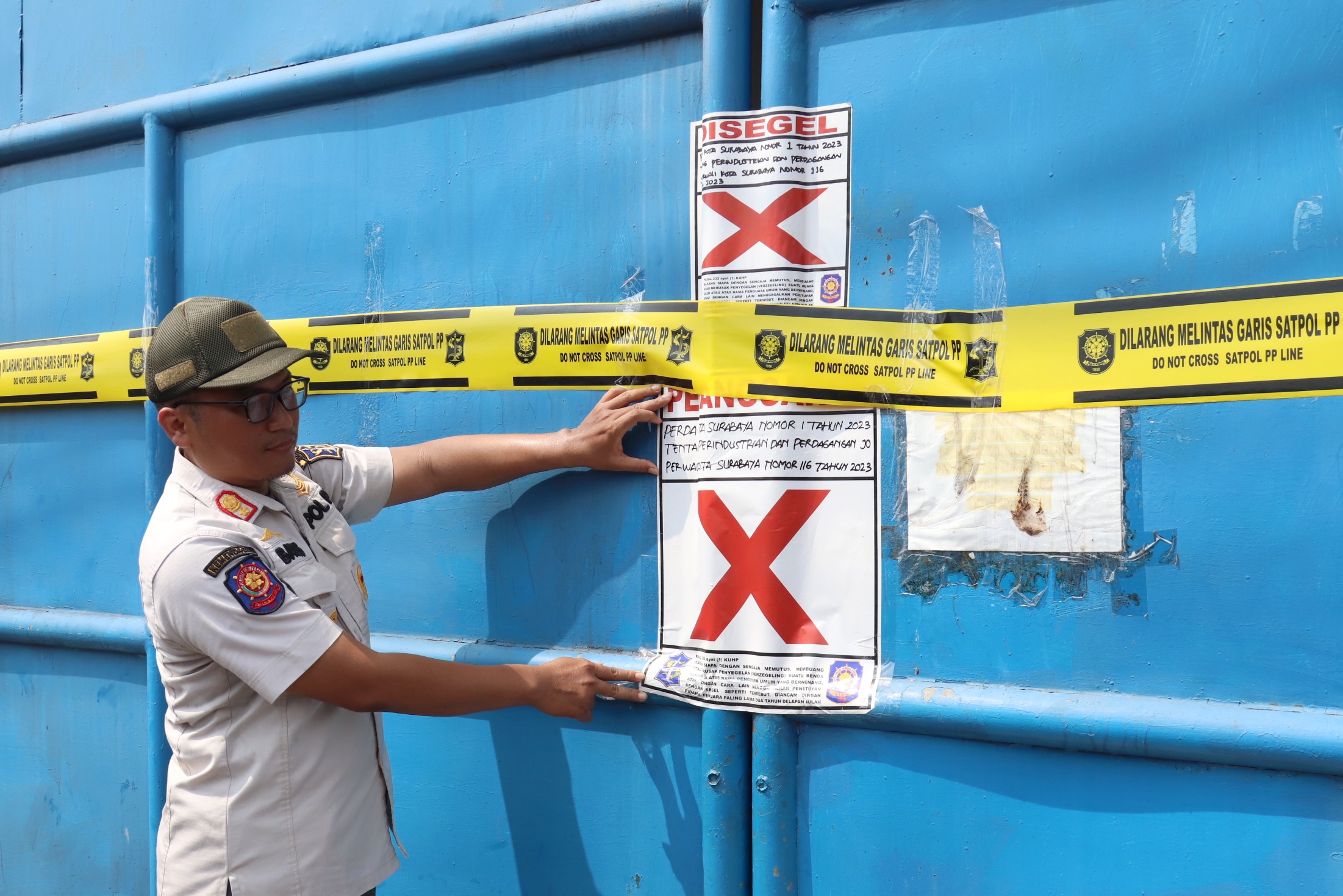 MELANGGAR: Petugas Satpol PP Surabaya memasang tanda penyegelan dan Satpol PP line di pintu gerbang utama gudang milik CV Sentoso Seal.