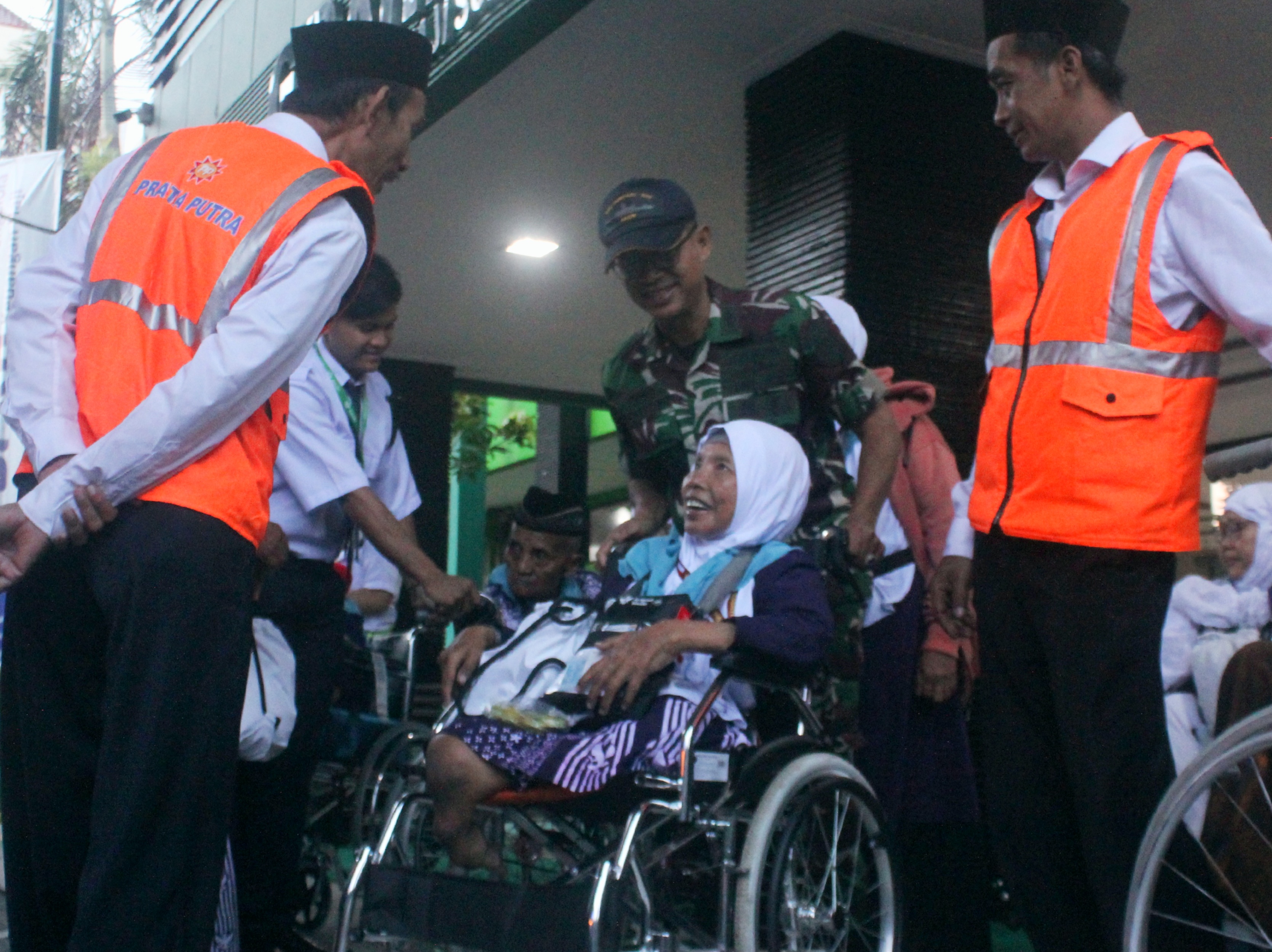 SEMANGAT: Muayatur saat dibantu petugas PPIH Embarkasi Surabaya menggunakan kursi roda menuju bus.