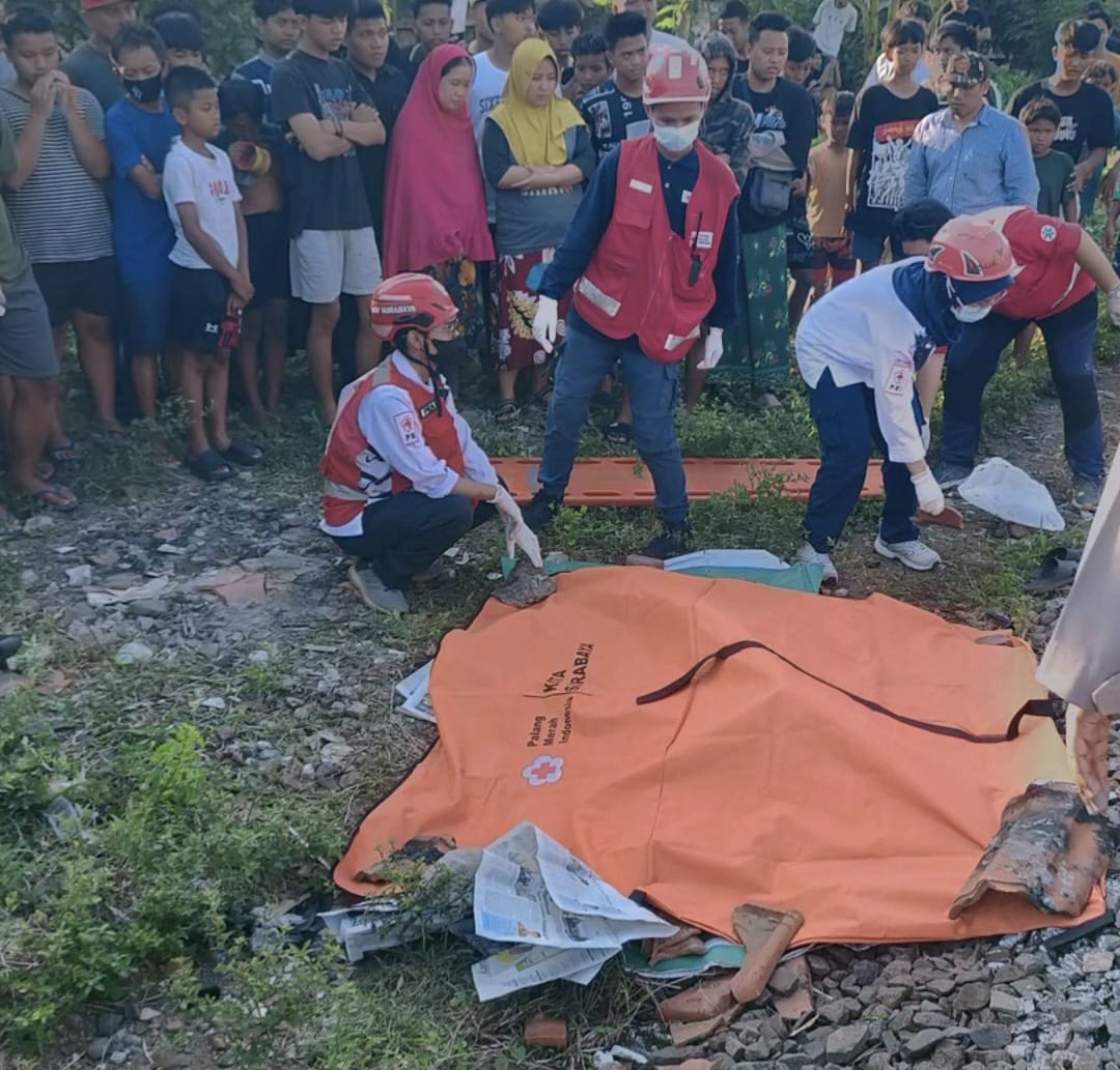 DIANGKAT : Petugas mengevakuasi jasad MS yang ditemukan meninggal dunia diduga akibat tertabrak KA di Jalan Kalibokor I, Surabaya. (IST/RADAR SURABAYA)