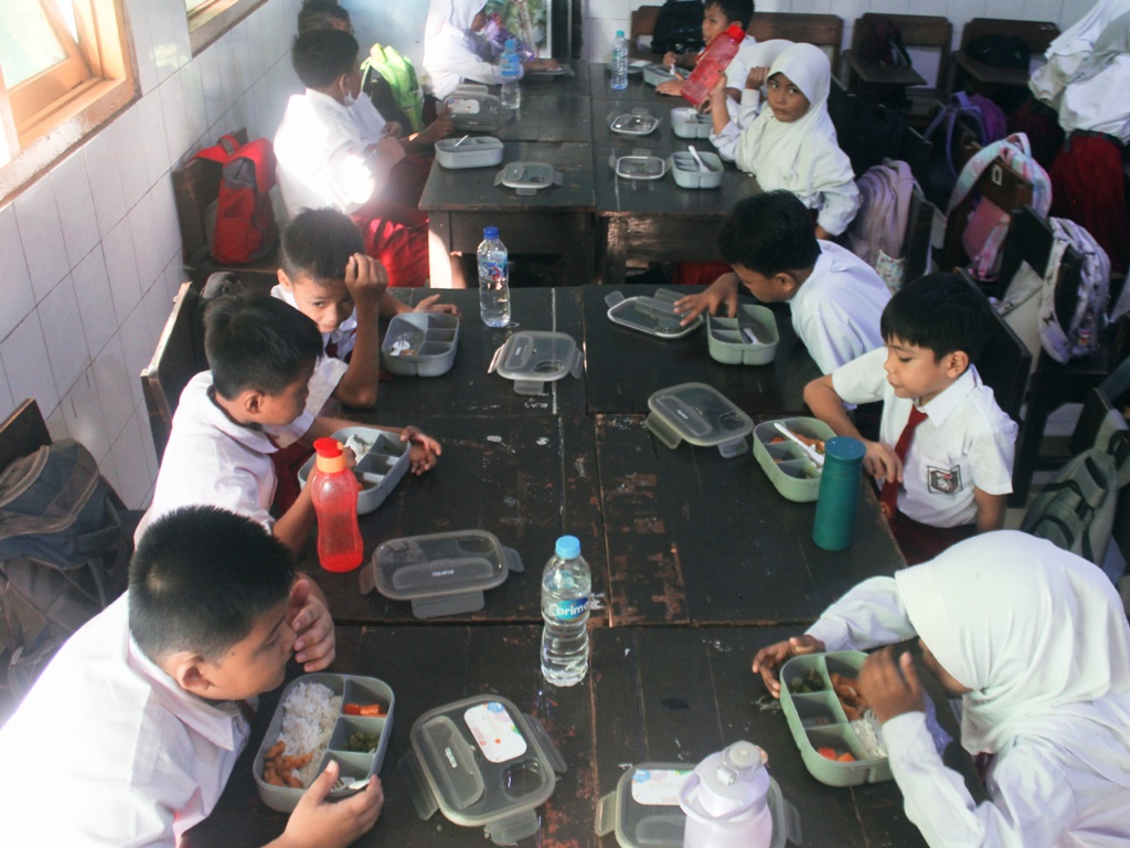 Murid-murid sekolah dasar menikmati makanan bergizi gratis. (RAHMAT SUDRAJAT/RADAR SURABAYA)