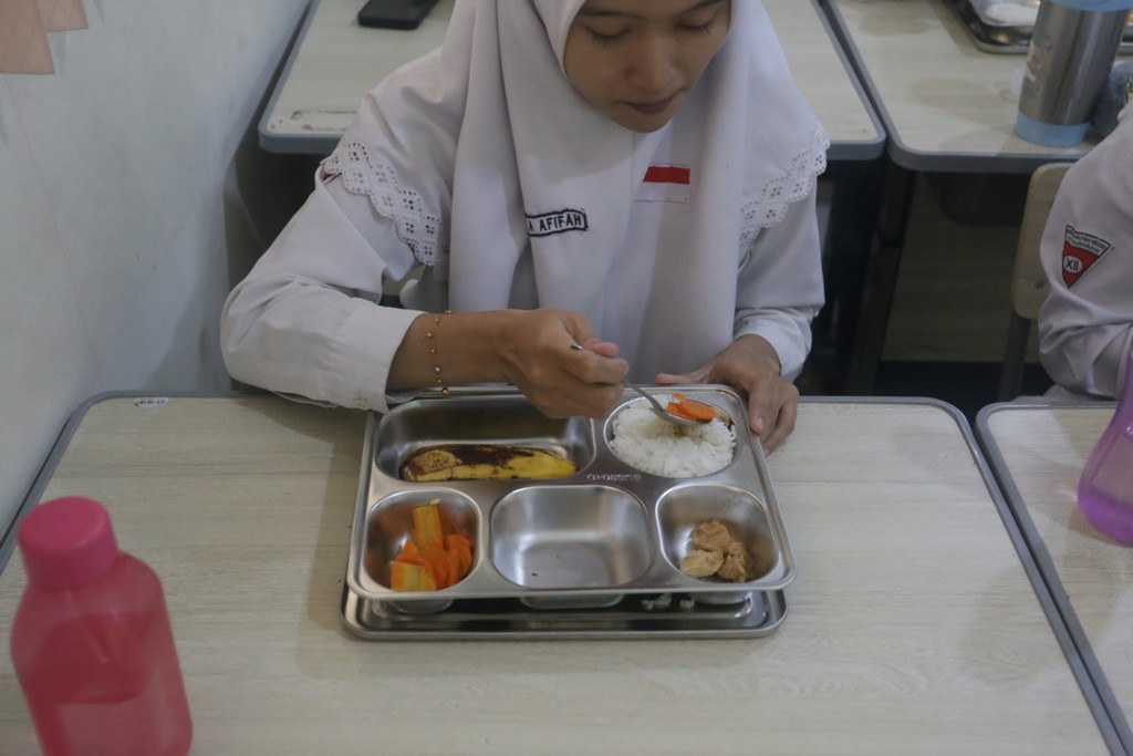 Seorang siswi menikmati makan bergizi gratis di Surabaya. (SURYANTO/RADAR SURABAYA)