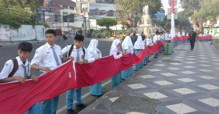 BERKOBAR: Pelajar di Kota Surabaya membentangkan bendera di depan Alun-alun Surabaya. Bendera sepanjang 15.400 meter ini dibentangkan dengan mengeliling pusat kota.