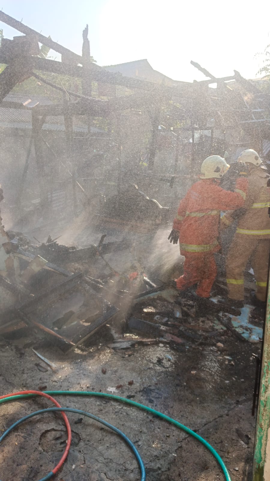 BERUPAYA: Petugas DPKP Surabaya melakukan pembasahan di rumah semipermanen Jalan Jemur Wonosari, Surabaya, yang terbakar, Selasa (23/9). (IST/RADAR SURABAYA)