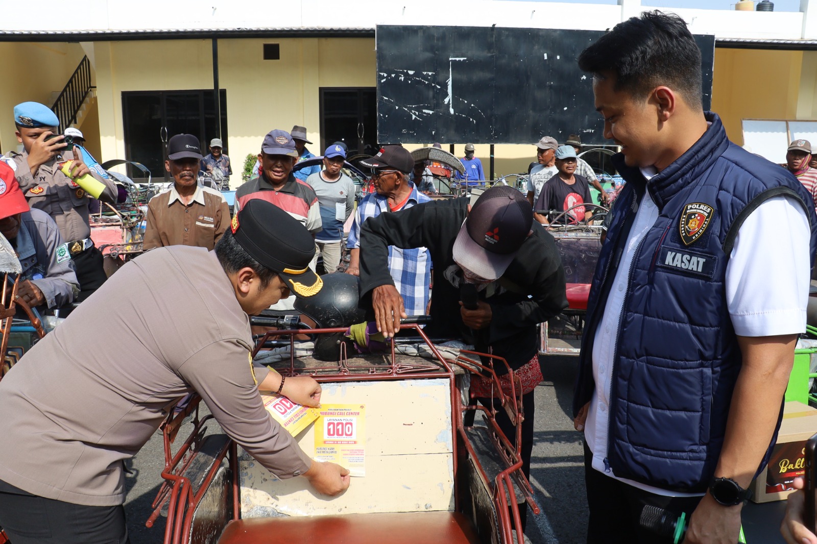 SOSIALISASI: Kapolres Pelabuhan Tanjung Perak AKBP Wahyu Hidayat saat menempelkan stiker layanan call center. Ratusan tukang becak geruduk kantor polisi merayakan HUT Reserse.(IST/RADAR SURABAYA)