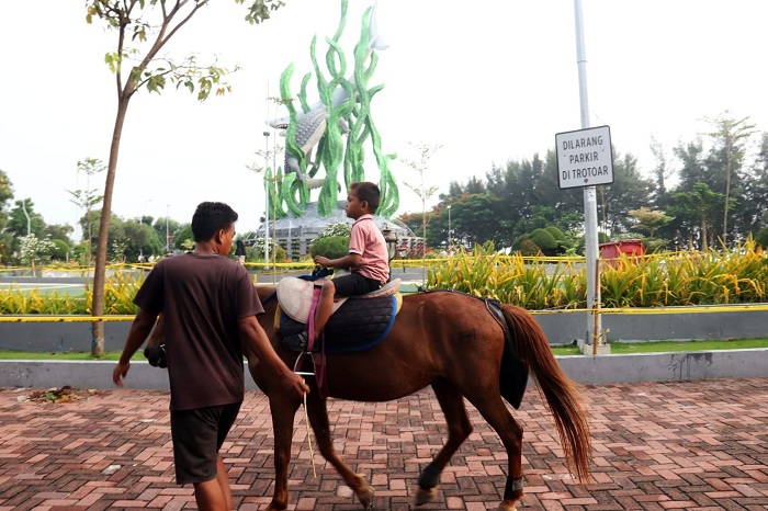 DAMPINGI PENGUNJUNG: Ashabul Khoir, mendampingi salah satu wisatawan yang menggunakan jasa tunggang kuda miliknya, di area Taman Suroboyo, Bulak.