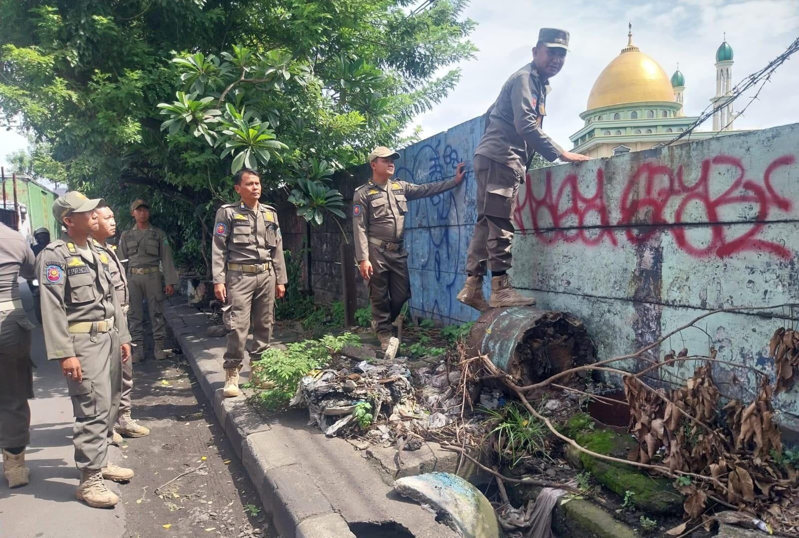LANCAR: Kepala Seksi Operasi dan Pengendalian (Kasi Opsdal) Satpol PP Sidoarjo, R. Novianto Koesno, AP memanjat dinding untuk melihat kondisi sekitar penertiban di Waru.