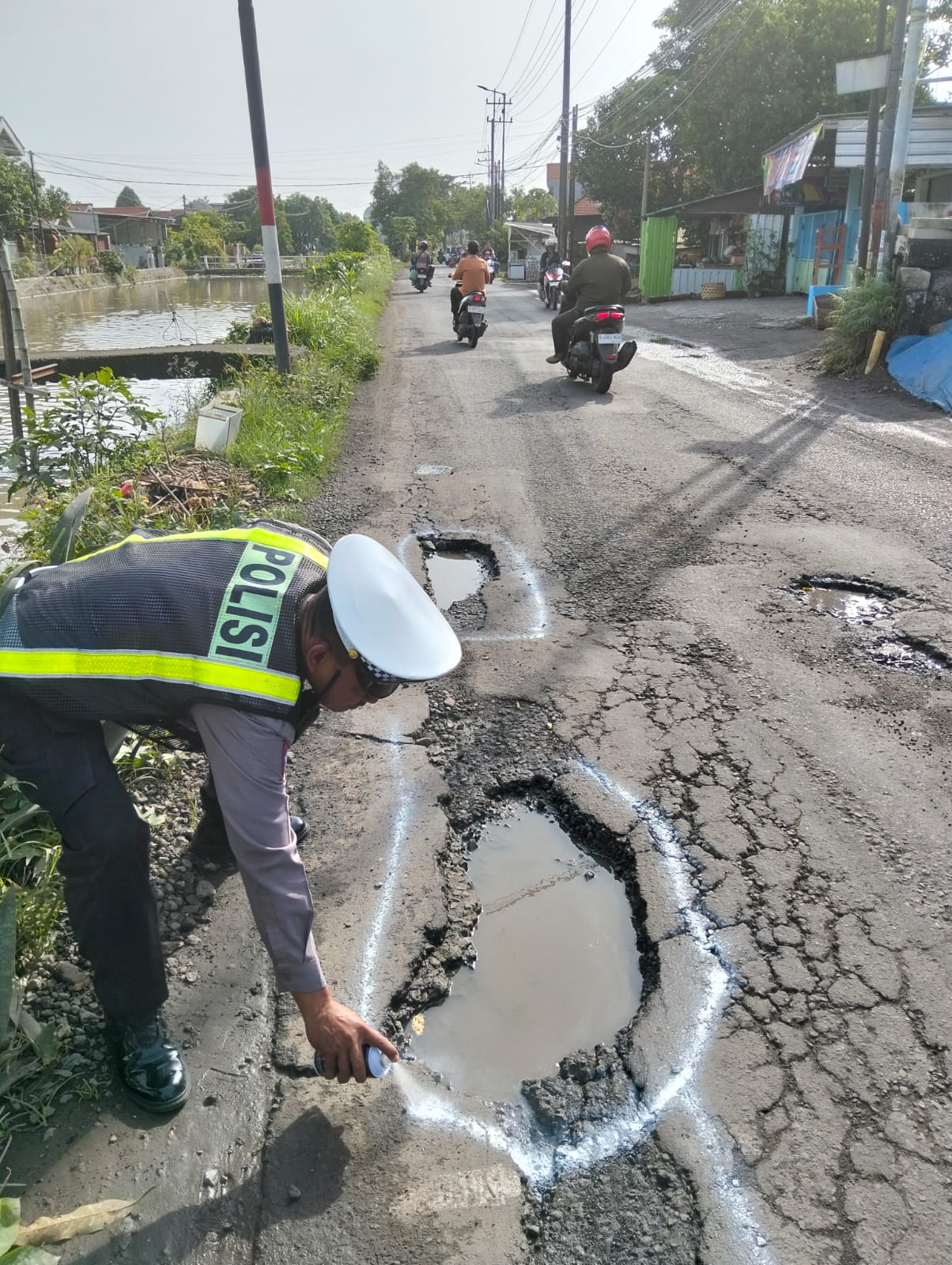 DITANDAI: Anggota lantas Polsek Taman saat memberi tanda pada jalan berlubang di Desa Tawangsari - Krembangan, Sidoarjo. (IST/RADAR SURABAYA)