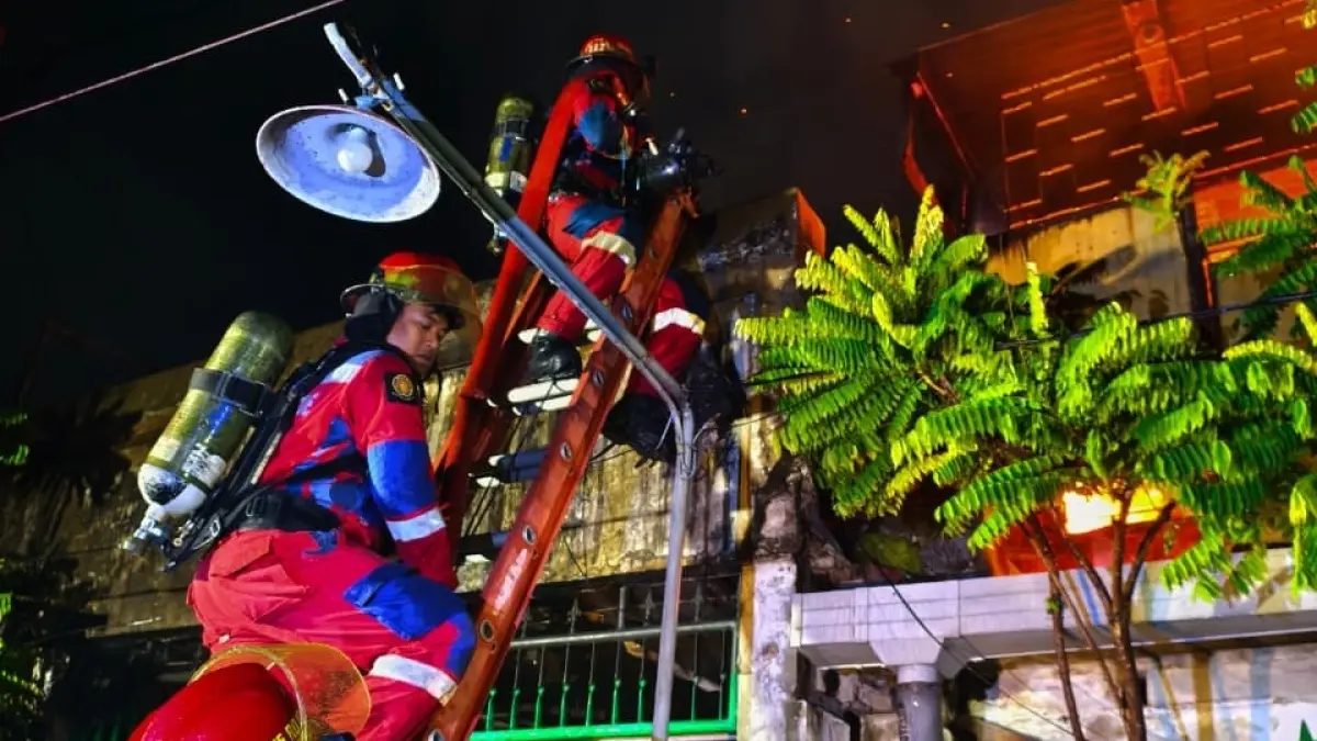 NAIK TANGGA: Petugas DPKP Surabaya saat melakukan pemadaman api yang membakar rumah konveksi milik Hoo Giok Liang di Jalan Sidoyoso II Gg 3 No.12-14, Surabaya, Senin (16/3). (Istimewa)