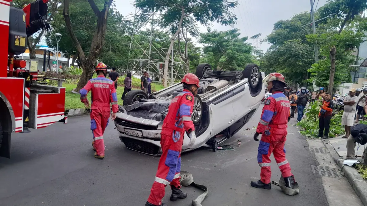 EVAKUASI: Petugas mengevakuasi mobil terbalik di Jalan Dharmahusada Indah, Surabaya. (IST/RADAR SURABAYA)