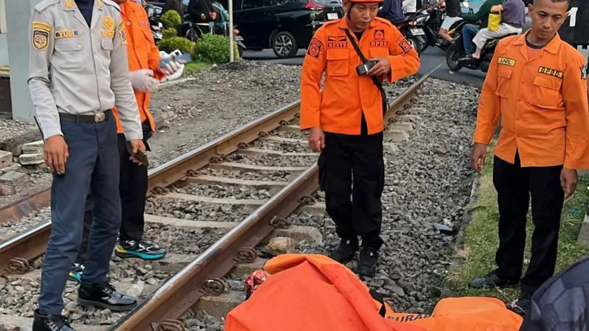 NAHAS: Petugas mengevakuasi jasad pengendara motor yang meninggal tertabrak KA di perlintasan Jalan Ahmad Yani, Surabaya. (IST/RADAR SURABAYA)
