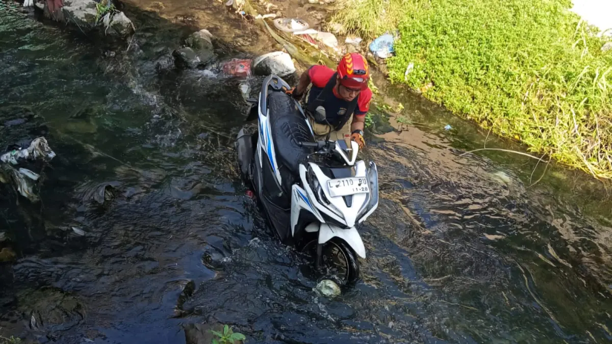 DIANGKAT: Petugas DPKP Surabaya saat mengevakuasi motor milik pengendara yang tercebur ke sungai Jalan Kupang Jaya, Surabaya. (IST/RADAR SURABAYA)