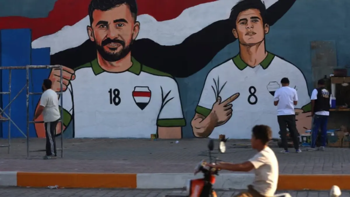 Sebuah mural yang menampilkan penyerang Irak, Aymen Hussein (kiri), terlihat di Sadr City, bagian timur Baghdad. Aymen Hussein sempat ditahan selama lebih dari tujuh jam saat tiba di Chicago. (The Guardian/Ahmad Al-Rubaye/AFP/Getty Images). 