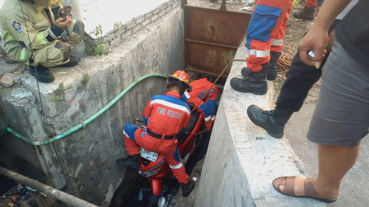 DIANGKAT: Petugas saat mengevakuasi motor korban yang masuk ke selokan di Jalan Pogot, Surabaya. (IST/RADAR SURABAYA)