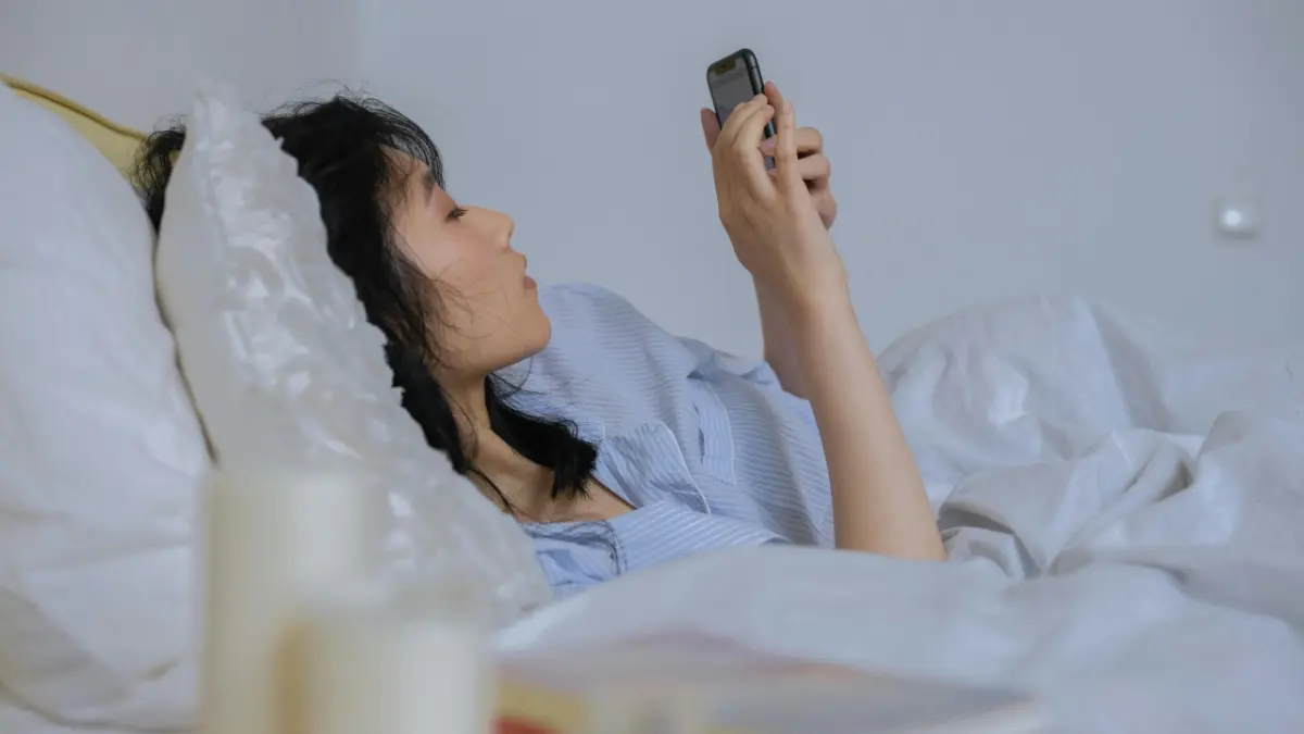 Ilustrasi seseorang membuka ponsel setelah bangun tidur. Penggunaan ponsel pada pagi hari sebaiknya tidak dilakukan secara berlebihan. Foto: Ist.