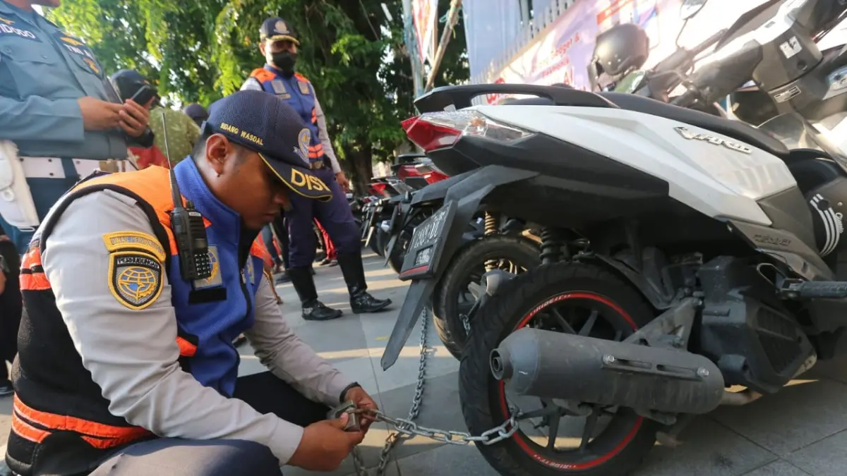 Petugas merantai motor yang parkir di jalur pedestrian Surabaya. (Andy Satria/Radar Surabaya)