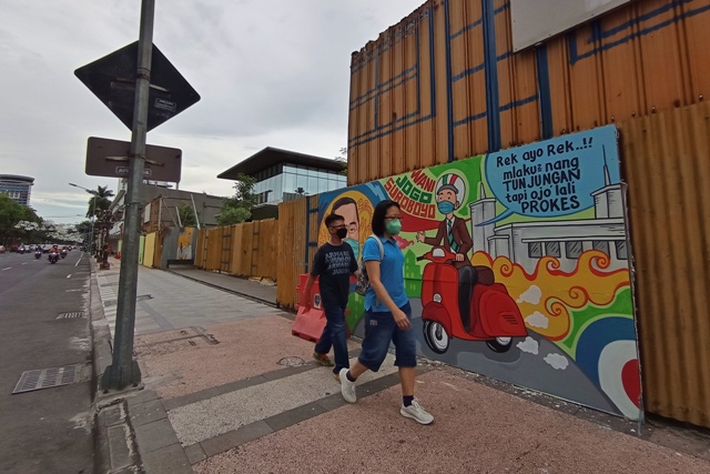 ADA PESANNYA: Pejalan kaki melintas tak jauh dari mural di kawasan Jalan Tunjungan, mural ini sengaja dibuat untuk mengkampanyekan protokol kesehatan, Minggu (31/10).  (SURYANTO/RADAR SURABAYA)