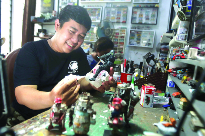 MAINAN SAMPAH: Adi Pradana saat membuat mainan figur dengan memanfaatkan barang bekas maupun sampah plastik di workshop-nya kawasan Wonorejo. (ANDY SATRIA/RADAR SURABAYA)