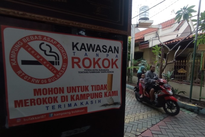 JAGA KESEHATAN: Warga melintas tak jauh dari imbauan larangan merokok di kampung tanpa asap rokok di Bulaksari, Surabaya, Rabu (8/6). (SURYANTO/RADAR SURABAYA)