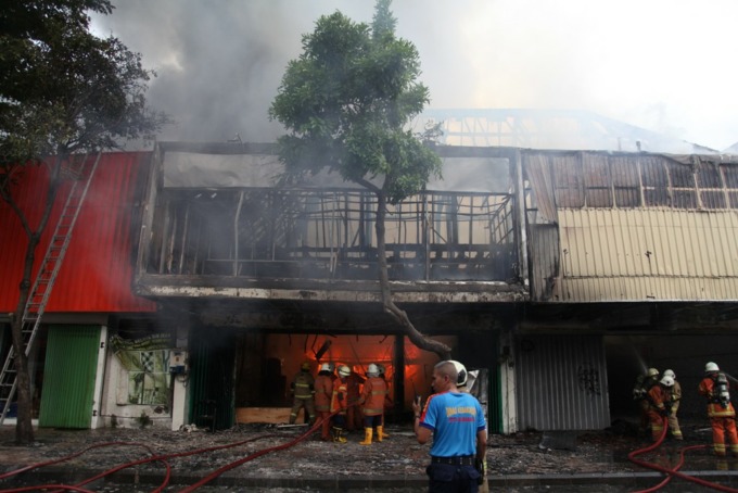 ASAP MENGEPUL: Petugas berusaha memadamkan api di salah satu toko karpet di Jalan Gemblongan, Surabaya, Minggu (16/10). (Suryanto/Radar Surabaya)