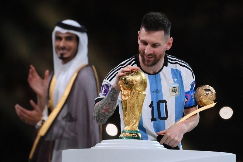 Pemain Argentina Lionel Messi menyentuh trofi Piala Dunia serta memegang penghargaan Bola Emas pada upacara penyerahan trofi Piala Dunia 2022 Qatar di Stadion Lusail, Doha pada 18 Desember 2022. (AFP/FRANCK FIFE)