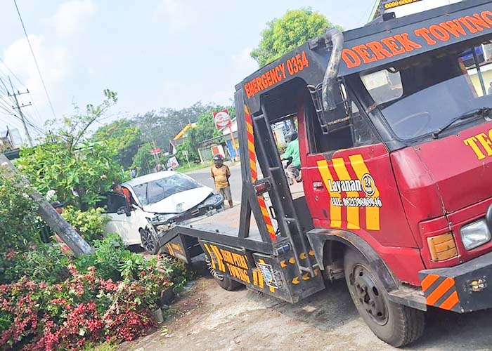 MIRING: Salah seorang warga mengamati kondisi tiang wifi di jalan raya Kediri-Kertosono masuk Desa Minggiran, Papar yang doyong usai ditabrak Honda Jazz.