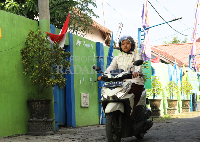 KURANG SISWA: Seorang pelajar melintas menggunakan sepeda motor di depan banner SMA Daha.