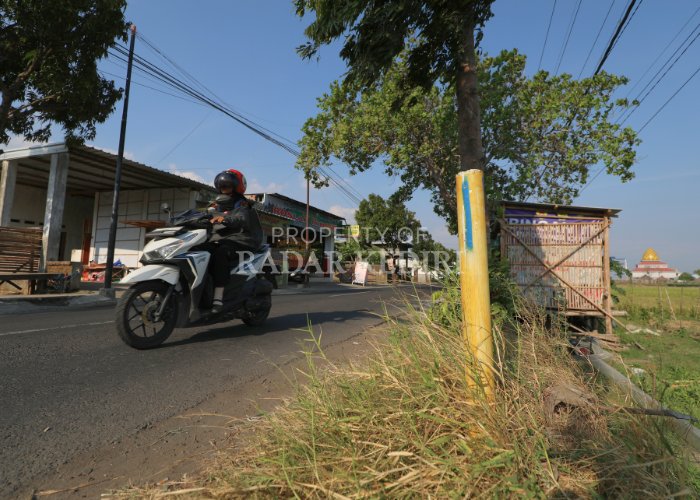 TUNGGU KEPASTIAN: Pengendara motor melintas dekat patok tol berwarna kuning yang ada di Kelurahan Gayam, Kecamatan Mojoroto.