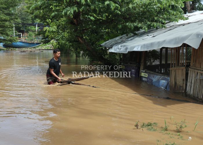 MELUAP: Seorang warga di Kelurahan Manisrenggo, Kecamatan Kota Kediri membersihkan material bambu dekat warung yang terseret sungai Brantas kemarin.