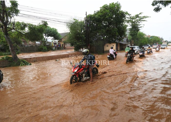 MELUBER KE JALAN: Air bercampur lumpur dari aliran Sungai Bendokrosok masuk ke Jl Raya Kediri-Nganjuk di Desa Maron, Banyakan. Akibatnya, pengendara harus mengurangi laju kendaraannya agar tak tergeli