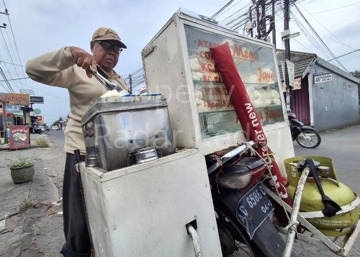 KENA DAMPAK: Pedagang  mengambil bakpau yang masih panas. Dia terpaksa menaikkan harga karena imbas perubahan HET elpiji.