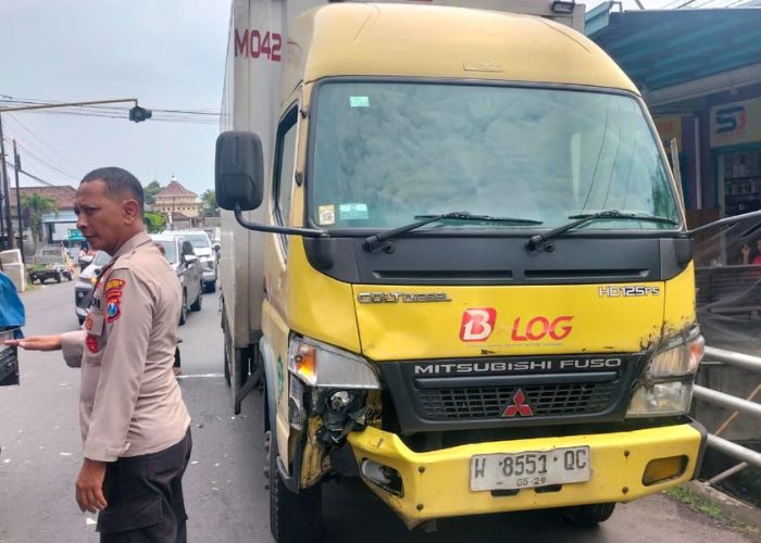PELAN-PELAN: Truk box yang terlibat laka parkir di tepi jalan. Seorang polisi dari Polres Kediri sedang mengatur lalu lintas kendaraan agar tidak mengebut.