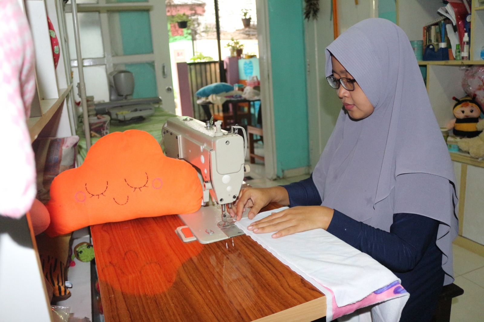 Khotamin sedang menjahit sarung bantal.