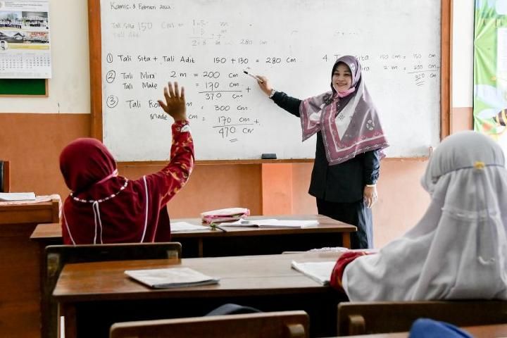 Seorang guru sedang mengajar siswa di kelas.