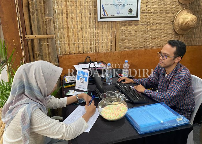 PELAYANAN EKSTRA: Petugas Dispendukcapil Kabupaten Kediri melayani pengunjung yang sedang mengisi formulir.