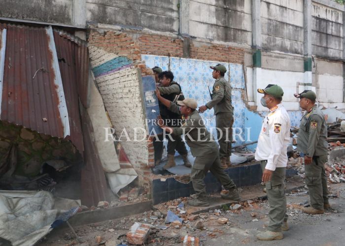 SEKUAT TENAGA: Petugas Satpol PP mendorong dinding yang dibangun permanen.