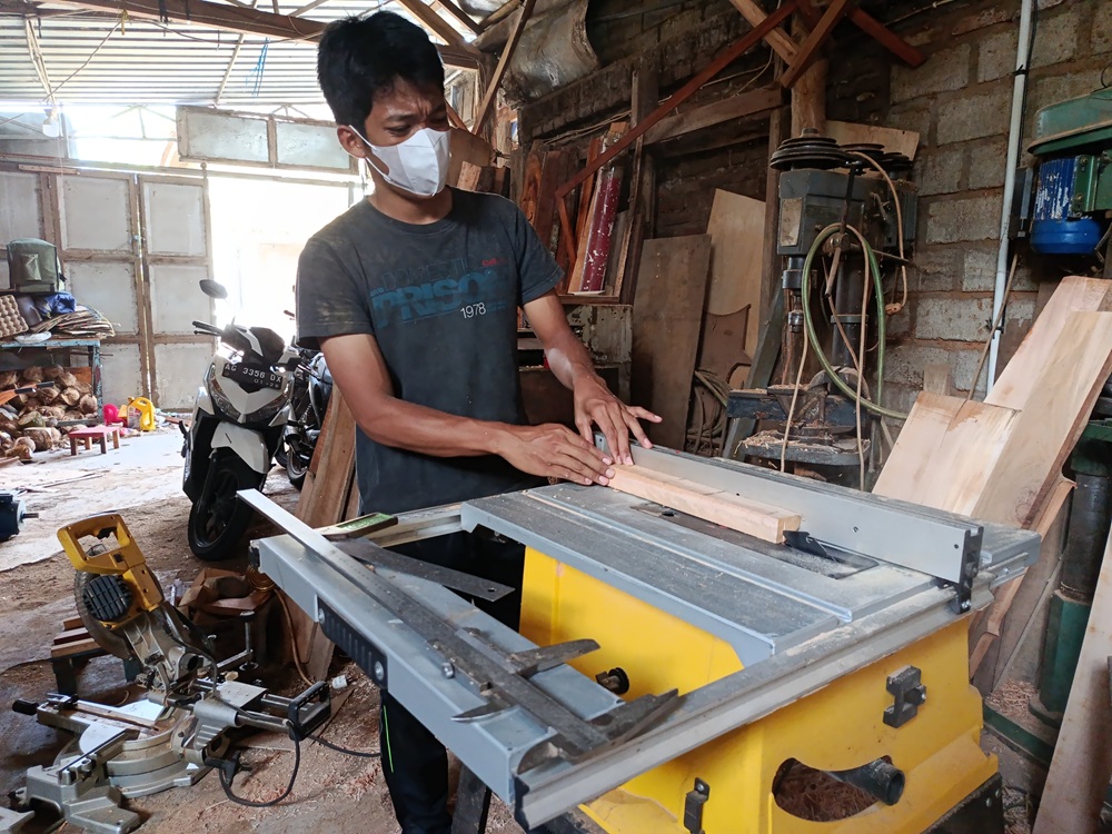 Khamim bekerja di bengkelnya membuat kerajinan dari kayu dengan alat CNC.