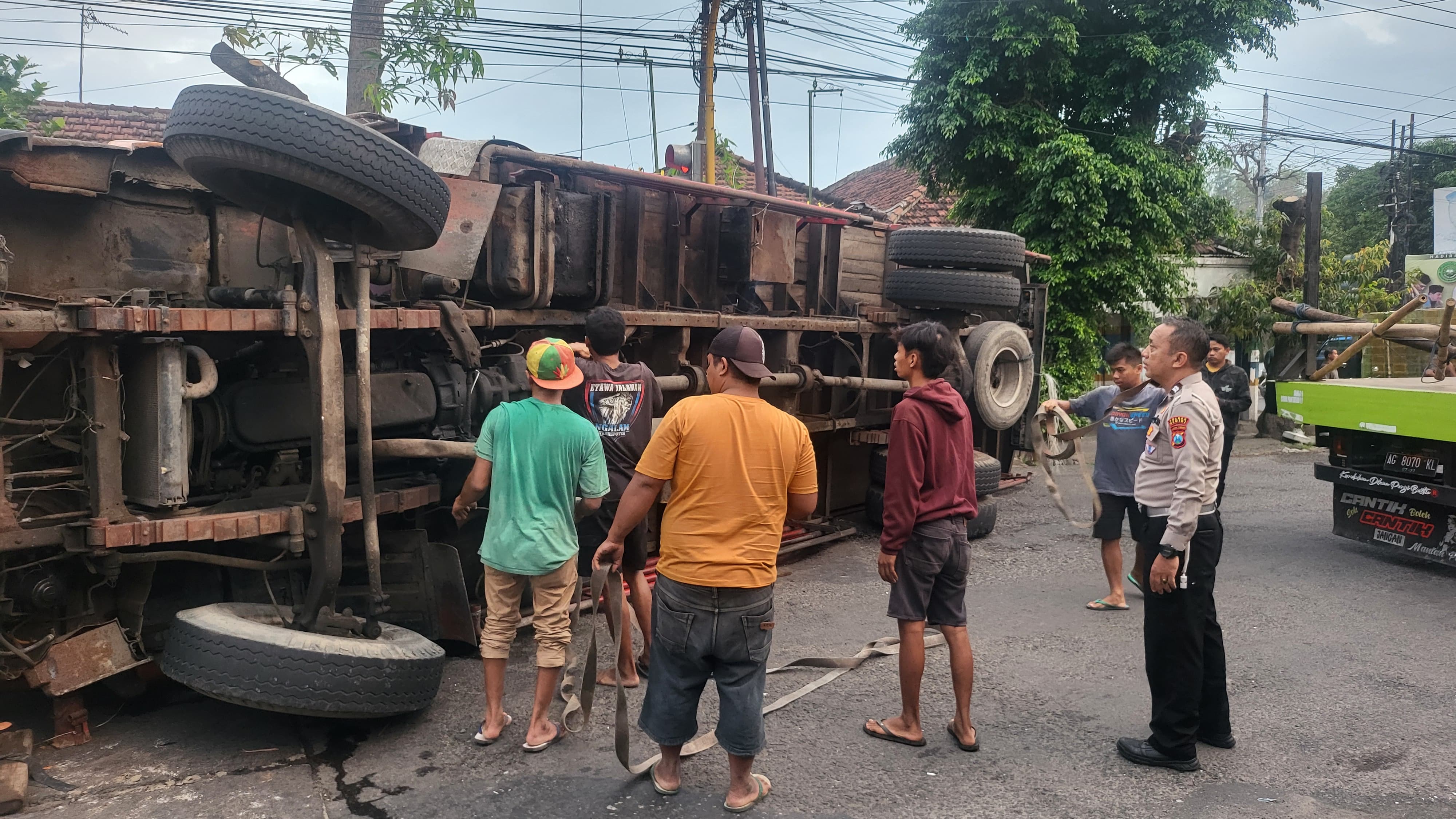 Polisi dan warga berusaha mengevakuasi truk yang terguling di jalan umum Desa Gedangsewu, Pare.