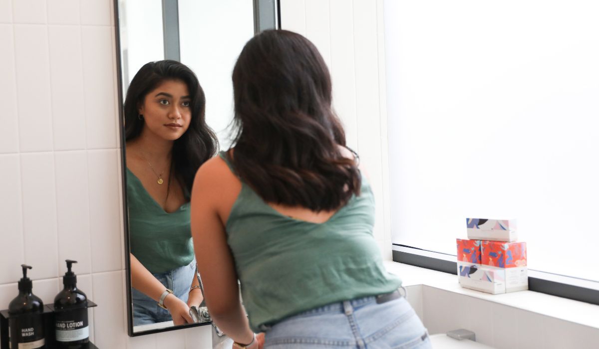 Wanita Melihat Dirinya di Cermin di Toilet Kantor Oleh Canva Studio Women
