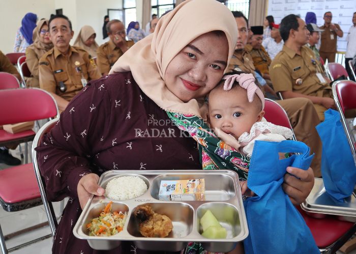 FULL SENYUM: Salah seorang ibu menyusui penerima MBG menunjukkan makanan yang didapatkannya di balai pertemuan Kelurahan Mrican.