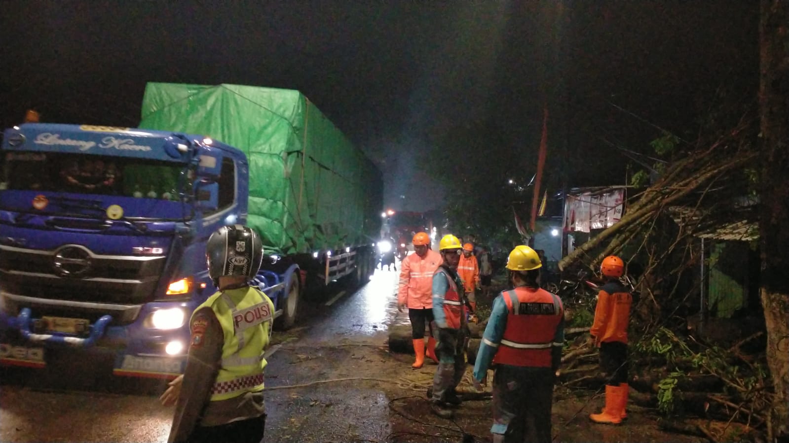 Anggota BPBD dan kepolisian melakukan pembersihan batang pohon yang tumbang .