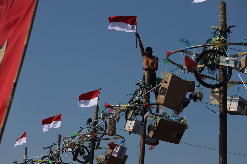 Peserta panjat pinang mengibarkan bendera ketika sampai di puncak.