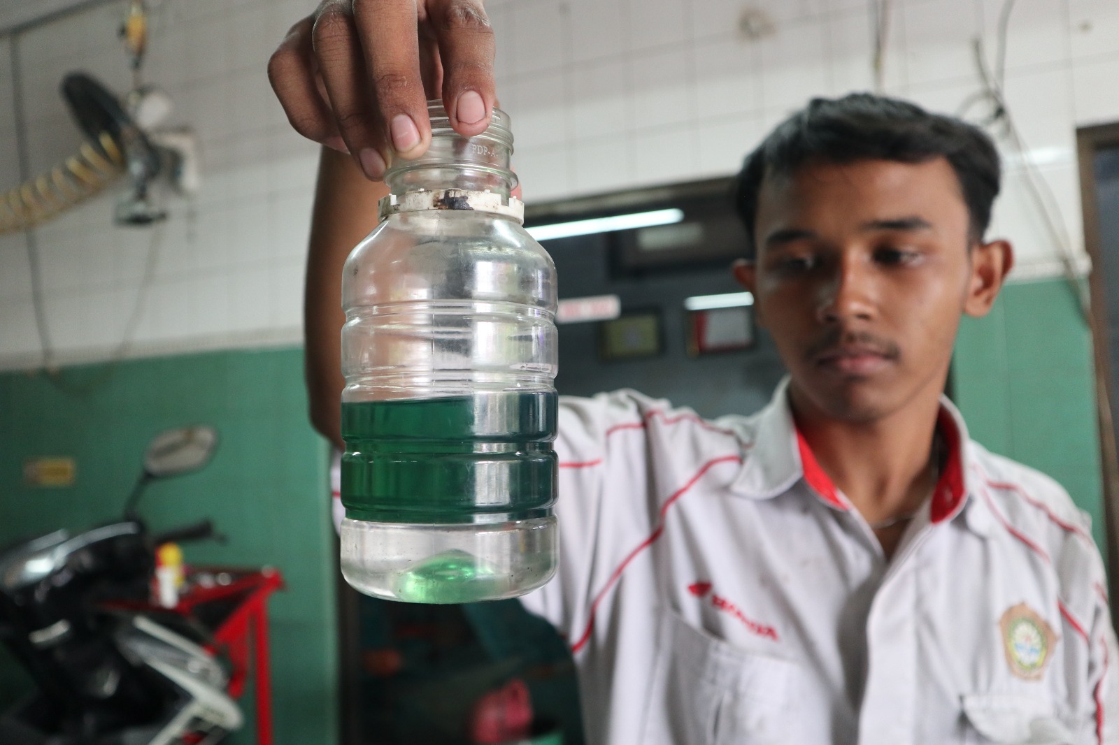 DUA LAPISAN: Mekanik bengkel di Jl Kilisuci menunjukkan endapan berwarna bening di BBM jenis pertalite dari motor pelanggan yang dimasukkan ke dalam botol kemarin.