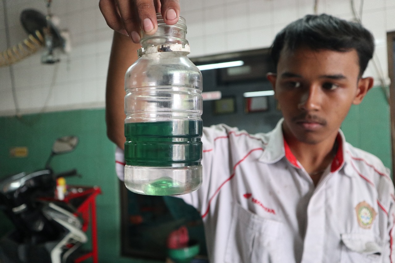 DUA LAPISAN: Mekanik bengkel di Jl Kilisuci menunjukkan endapan berwarna bening di BBM jenis pertalite dari motor pelanggan yang dimasukkan ke dalam botol kemarin.