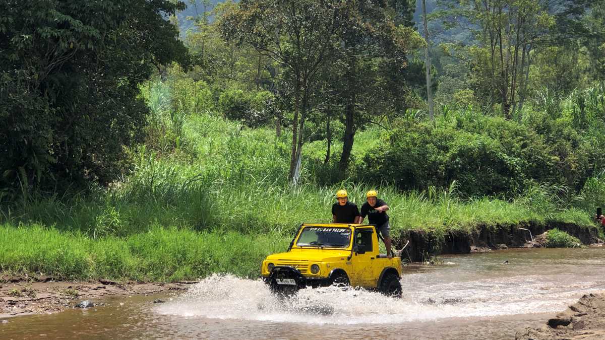 Mobil Jip Taft melintasi genangan lumpur dan sungai dangkal di jalur Fun Offroad Batu yang aman untuk pemula dan rombongan kantor.